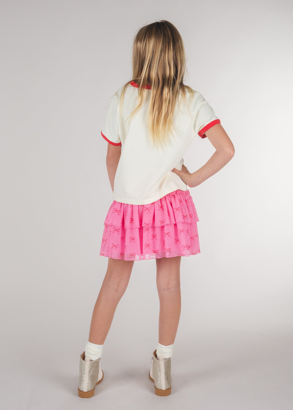 Back view of tween girl in a pink bow-print ruffle skirt and white tee