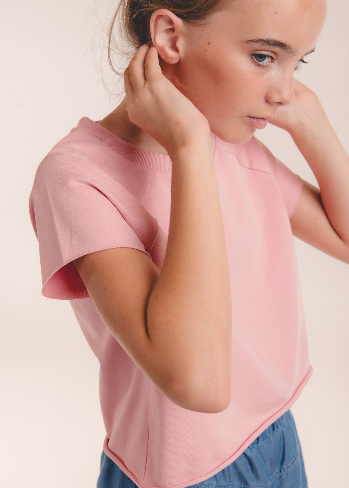 Detail of tween girl's shoulder in a solid pink crew-neck top