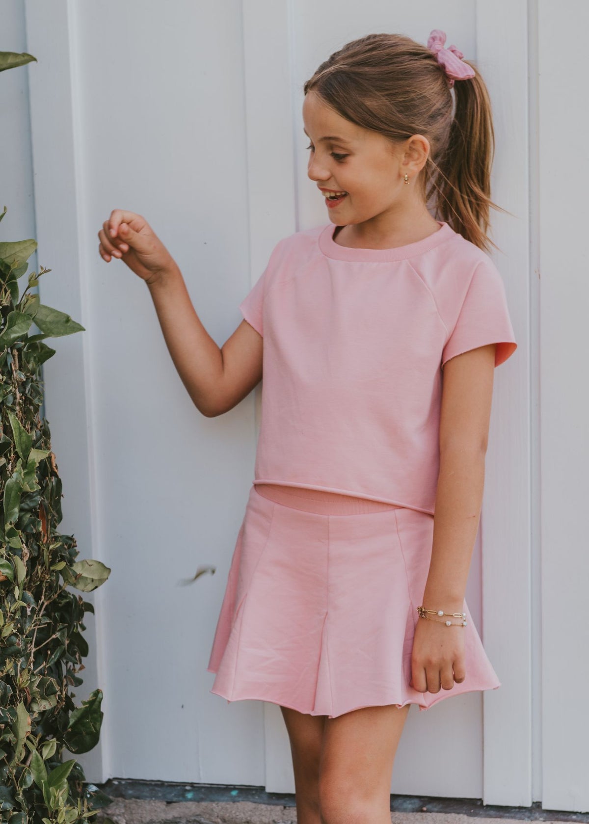 Tween girl wearing a solid pink top with matching pink pleated skort outdoors