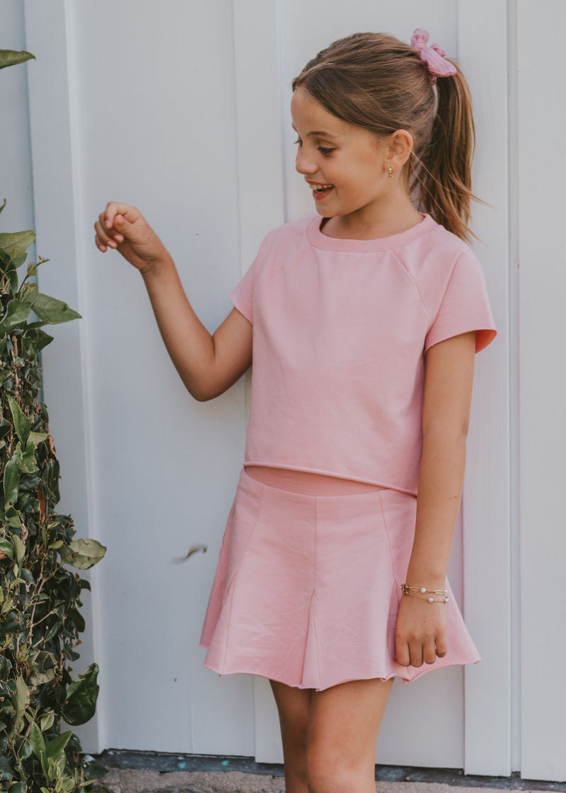 Tween girl wearing a solid pink top with matching pink pleated skort outdoors