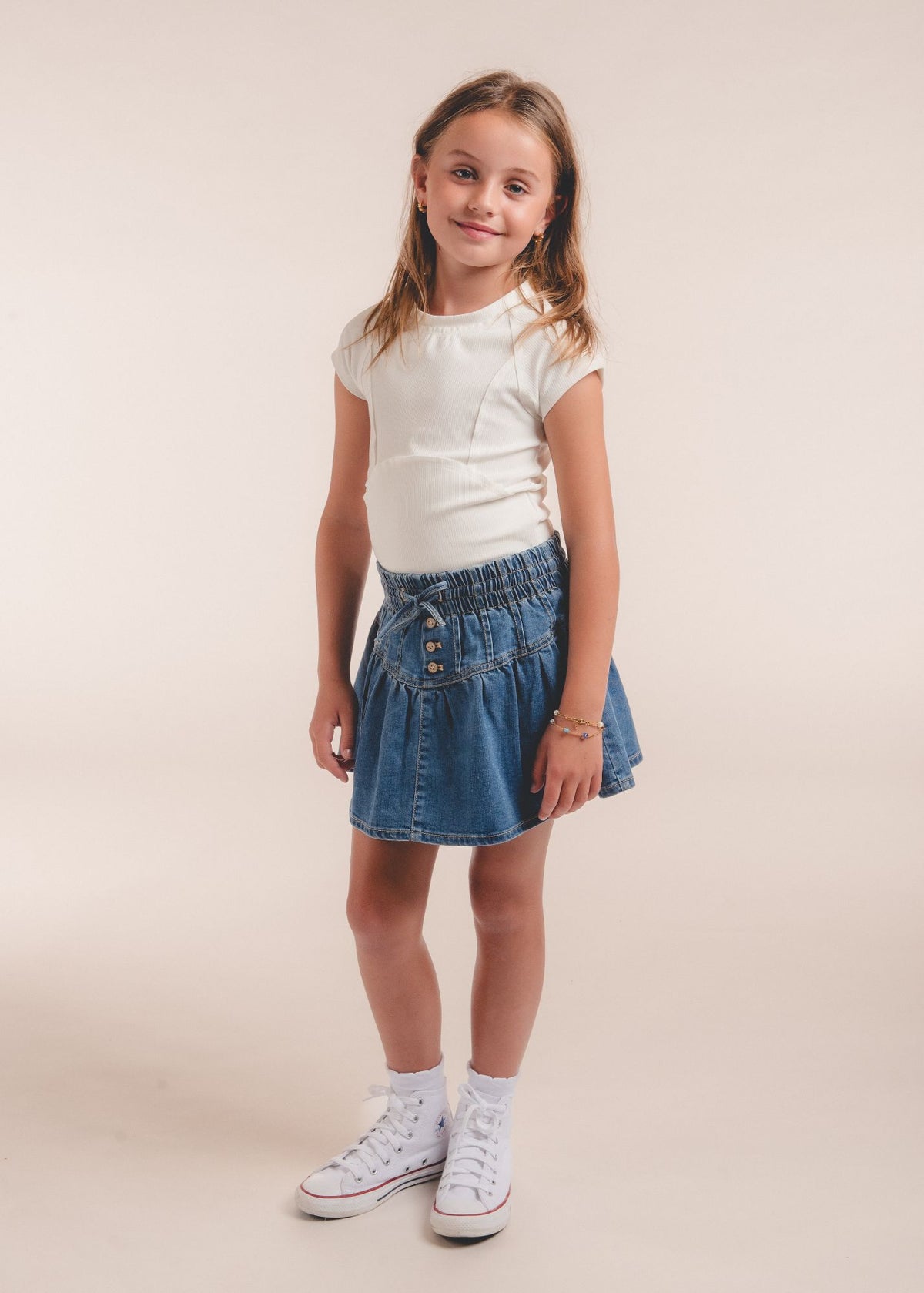 Tween girl wearing a blue denim skort with smocked waistband and white tee