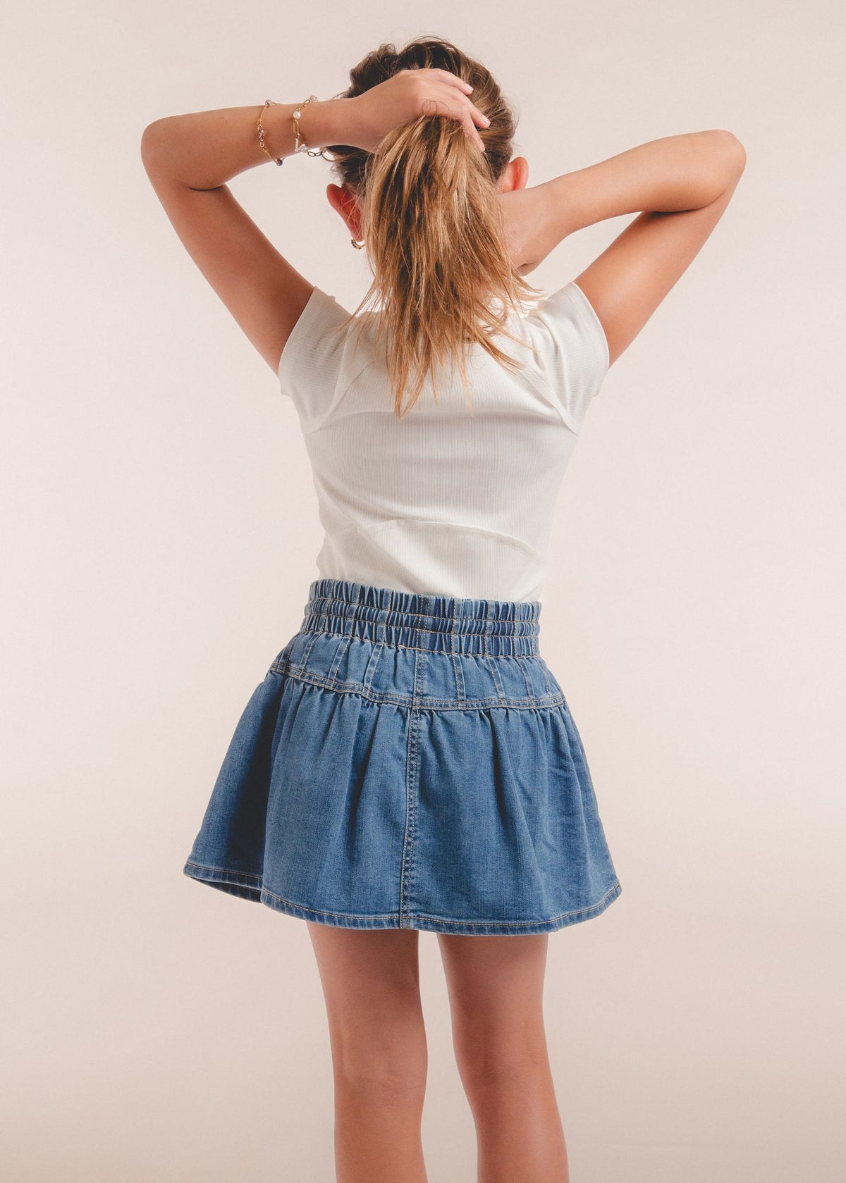 Tween girl wearing a blue denim skort from behind with smocked waistband