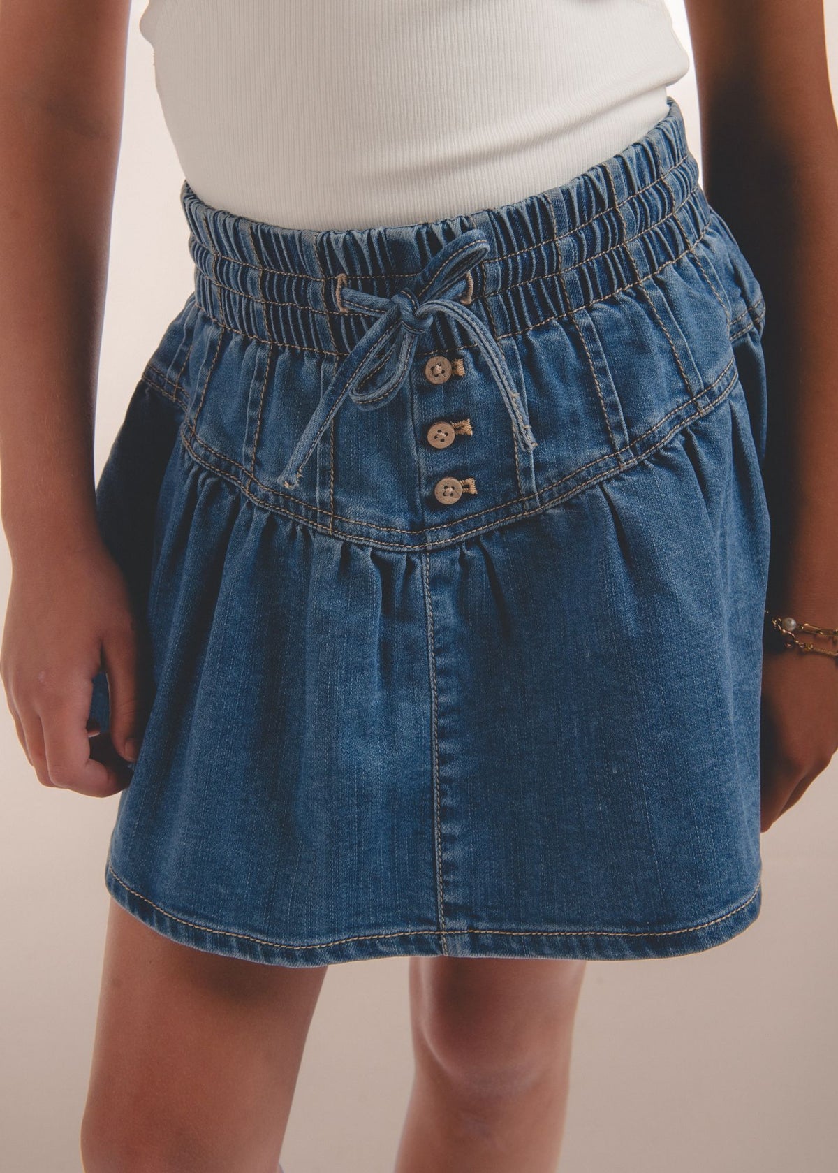 Close-up of blue denim skort waistband bow tie and button placket detail