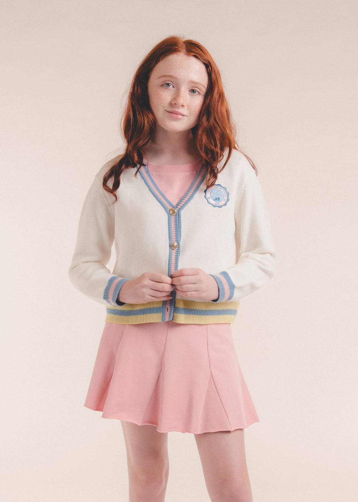 Tween girl wearing an ivory cardigan with striped trim, close-up portrait with pink skirt