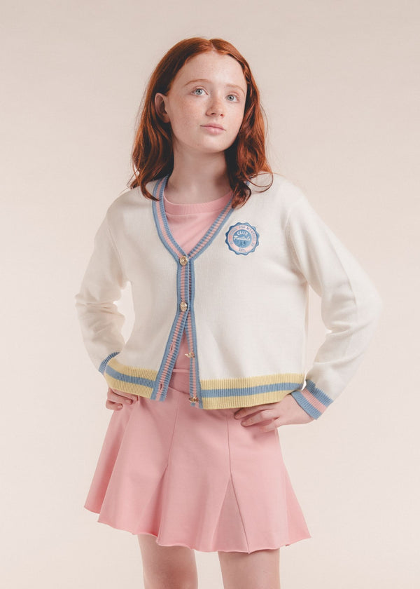 Tween girl wearing an ivory cardigan with blue and pink striped trim and pink skirt