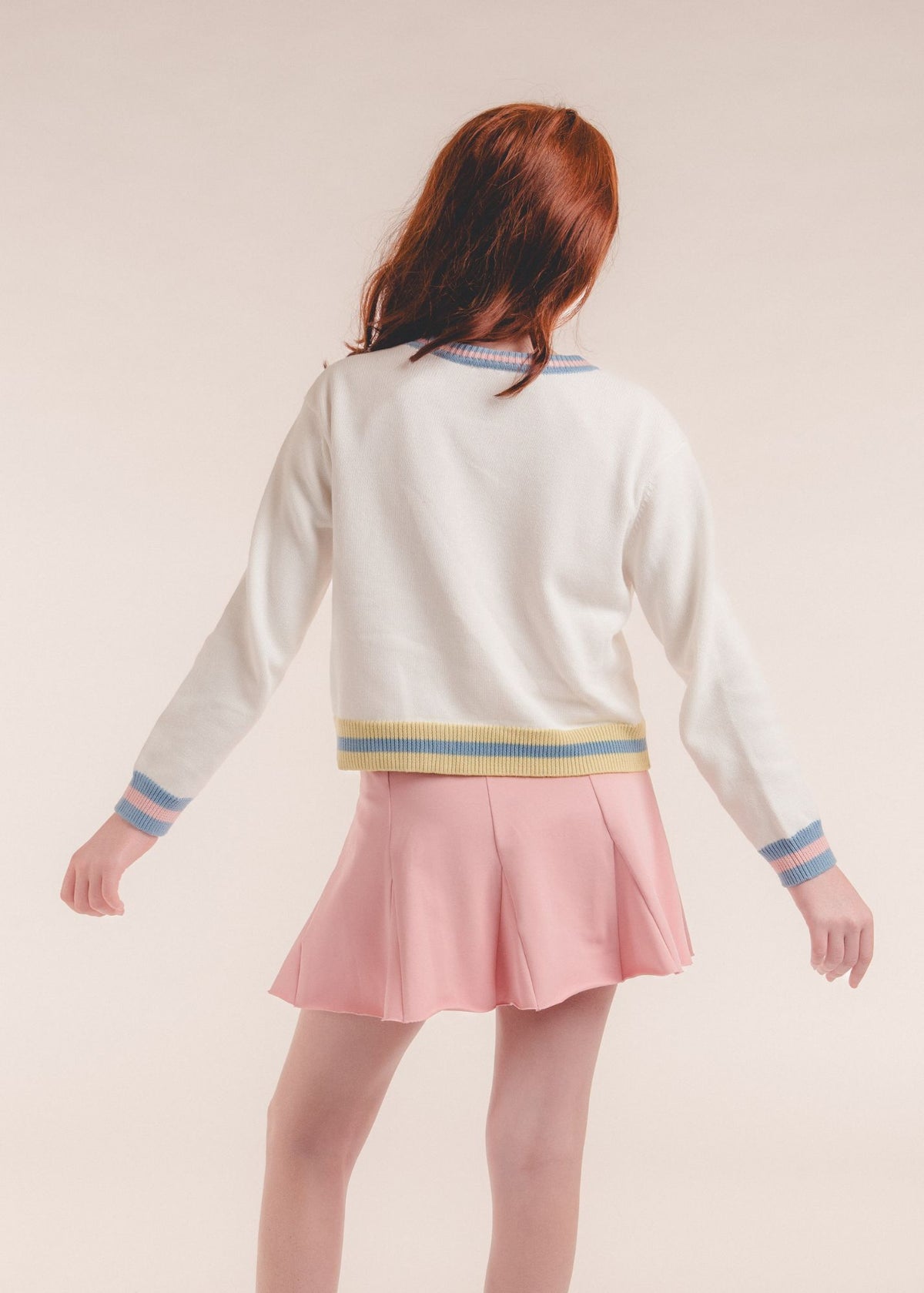 Back view of tween girl wearing an ivory cardigan with striped ribbed cuffs and hem