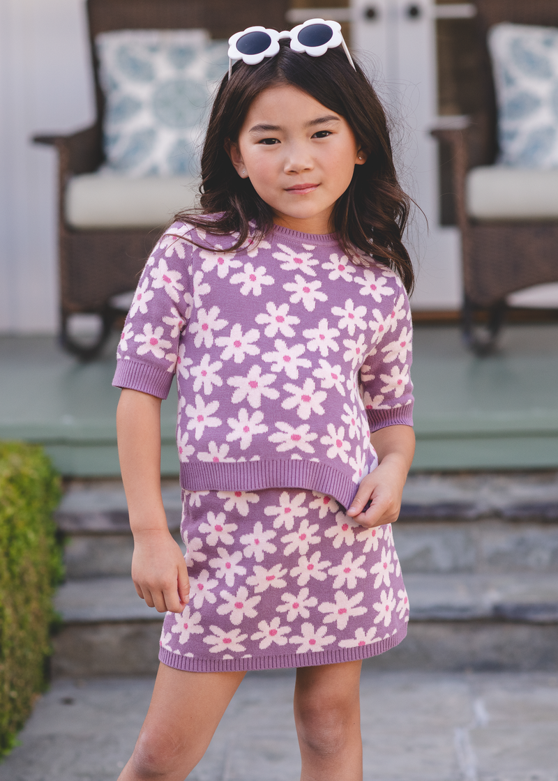 Tween girl wearing a purple daisy-print knit mini skirt and top on a porch