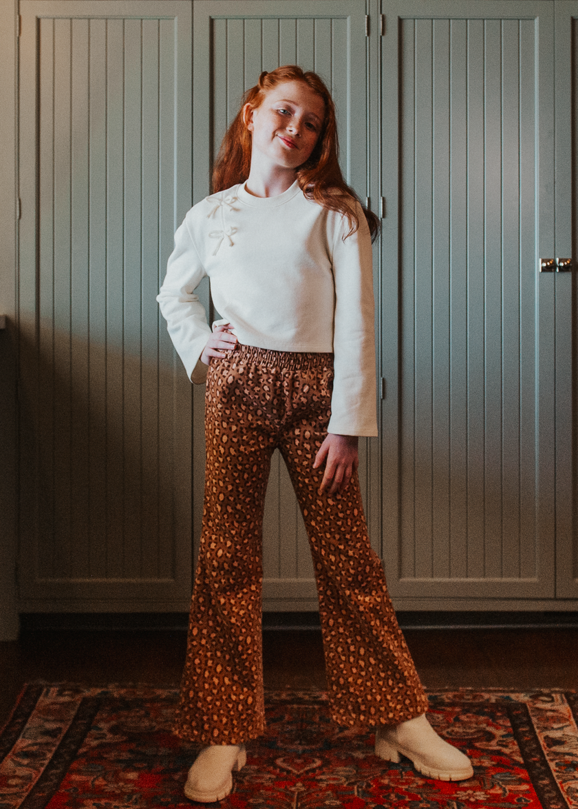 Tween girl wearing brown leopard print flared trousers with a white cropped sweater