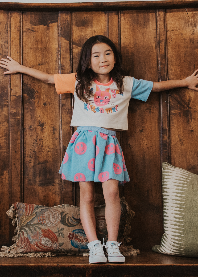 Tween girl wearing a blue tulle skirt with pink smiley print and a graphic tee