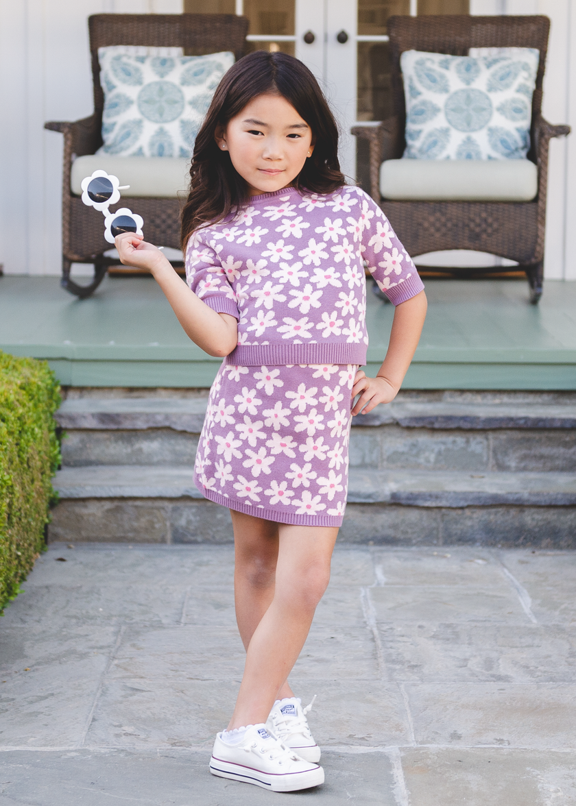 Tween girl wearing a purple daisy-print knit sweater top and matching skirt on a porch