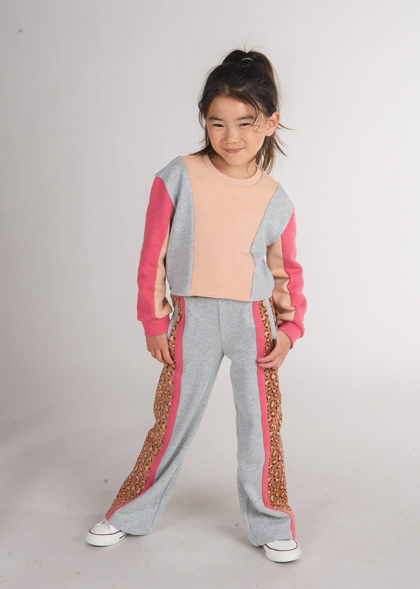 Tween girl wearing a peach and grey colorblock sweatshirt with pink side panels and leopard-print pants
