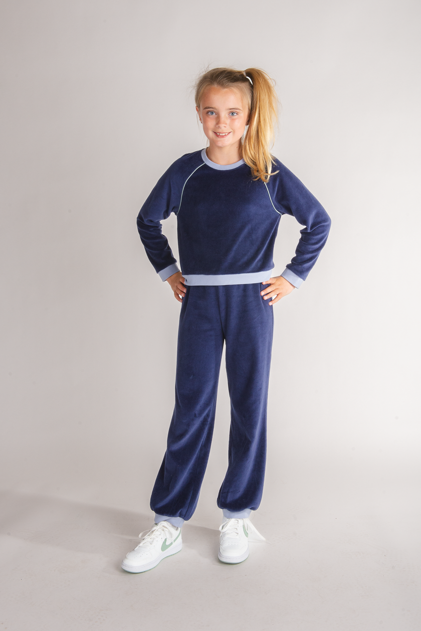 Tween girl wearing navy velour jogger bottoms with light blue cuffs and matching sweatshirt
