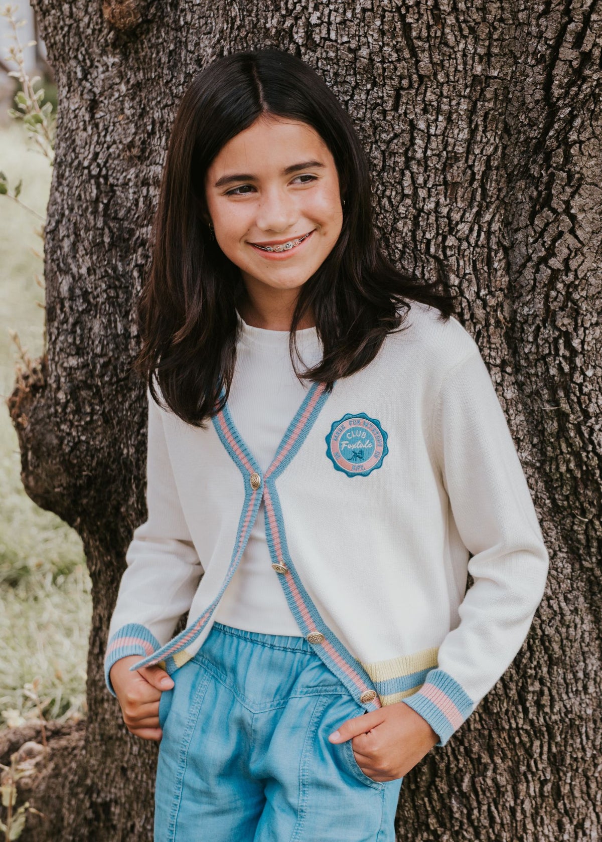 Tween girl wearing an ivory cardigan with striped trim styled with blue jeans outdoors