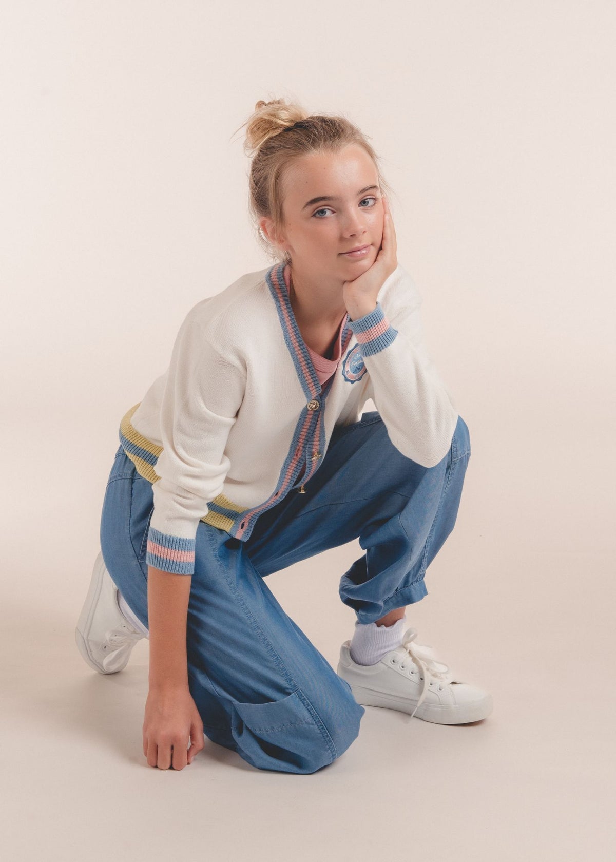 Tween girl kneeling in blue chambray jogger pants and white striped cardigan resting chin on hand