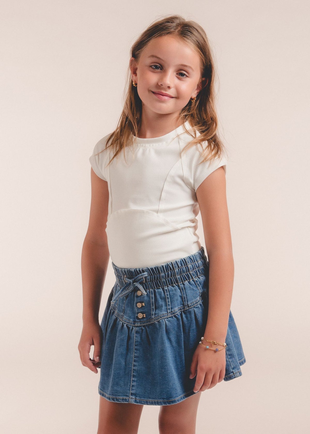 Tween girl wearing white cap-sleeve top with denim button-front skirt, smiling