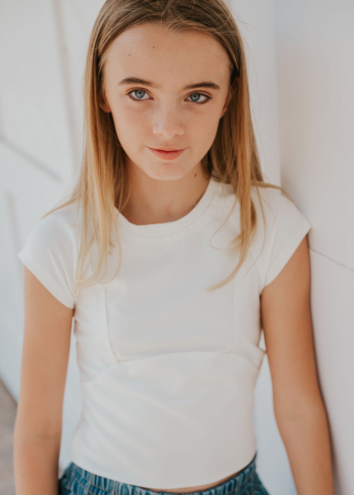 Close-up portrait of tween girl wearing white cap-sleeve top against white wall