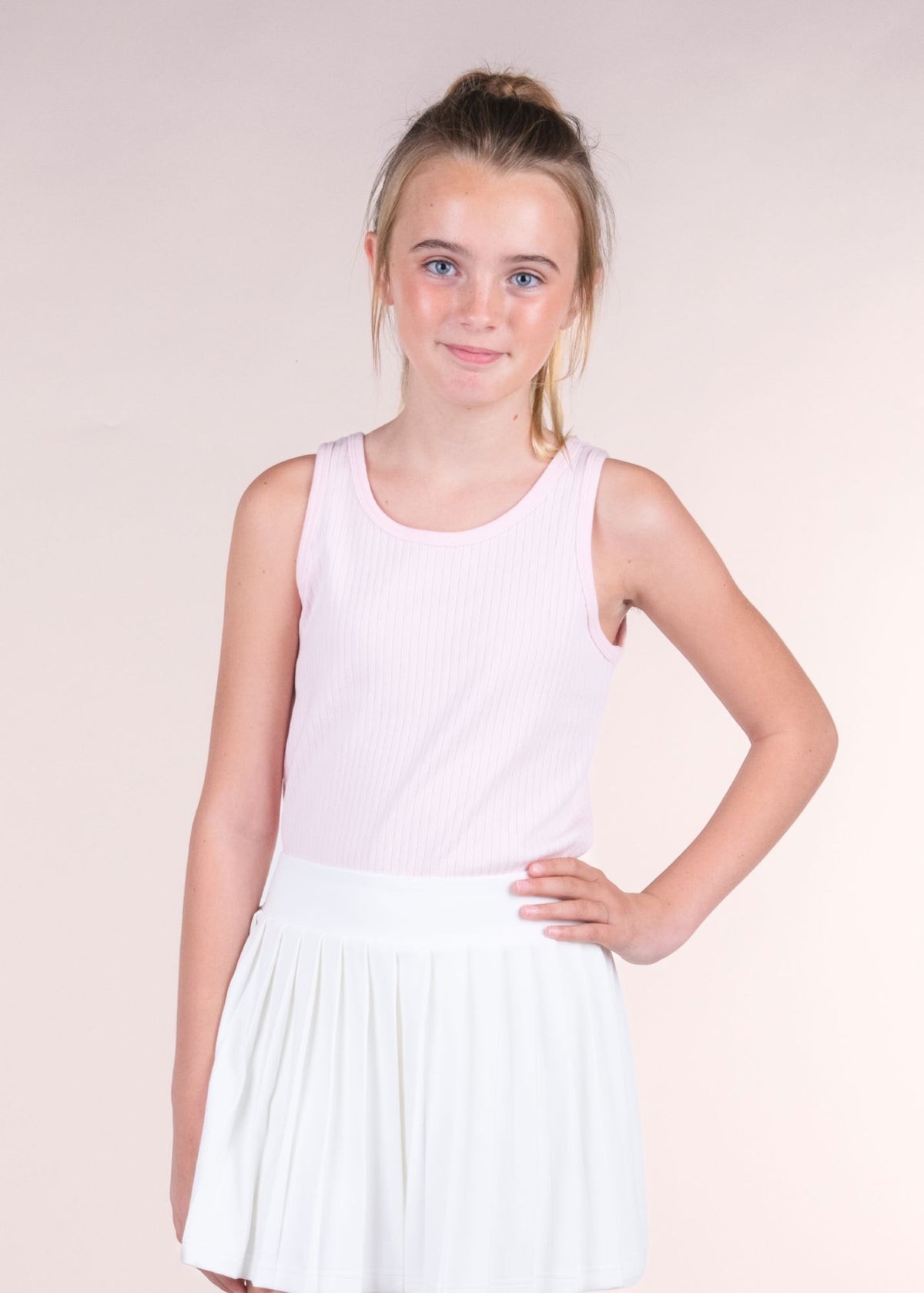 Tween girl wearing a blush pink ribbed tank top with hand on hip facing forward
