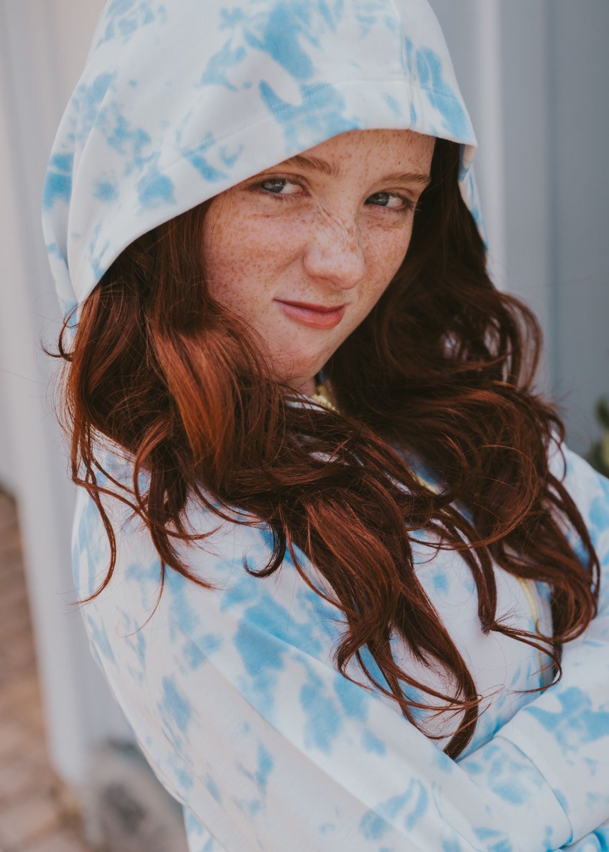 Young woman, hood up, arms crossed, wearing blue-and-white tie-dye zip-up hoodie