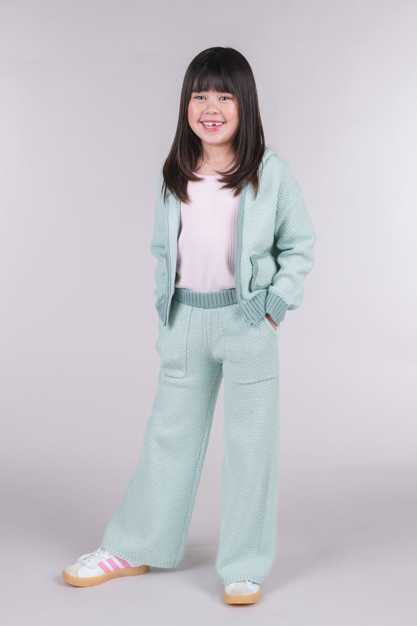 Tween girl wearing seafoam green knit sweater pants with a matching hooded cardigan
