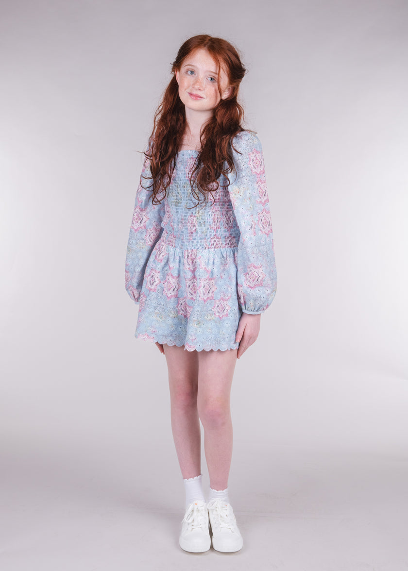Tween girl wearing a floral smocked long-sleeve romper in blue and pink