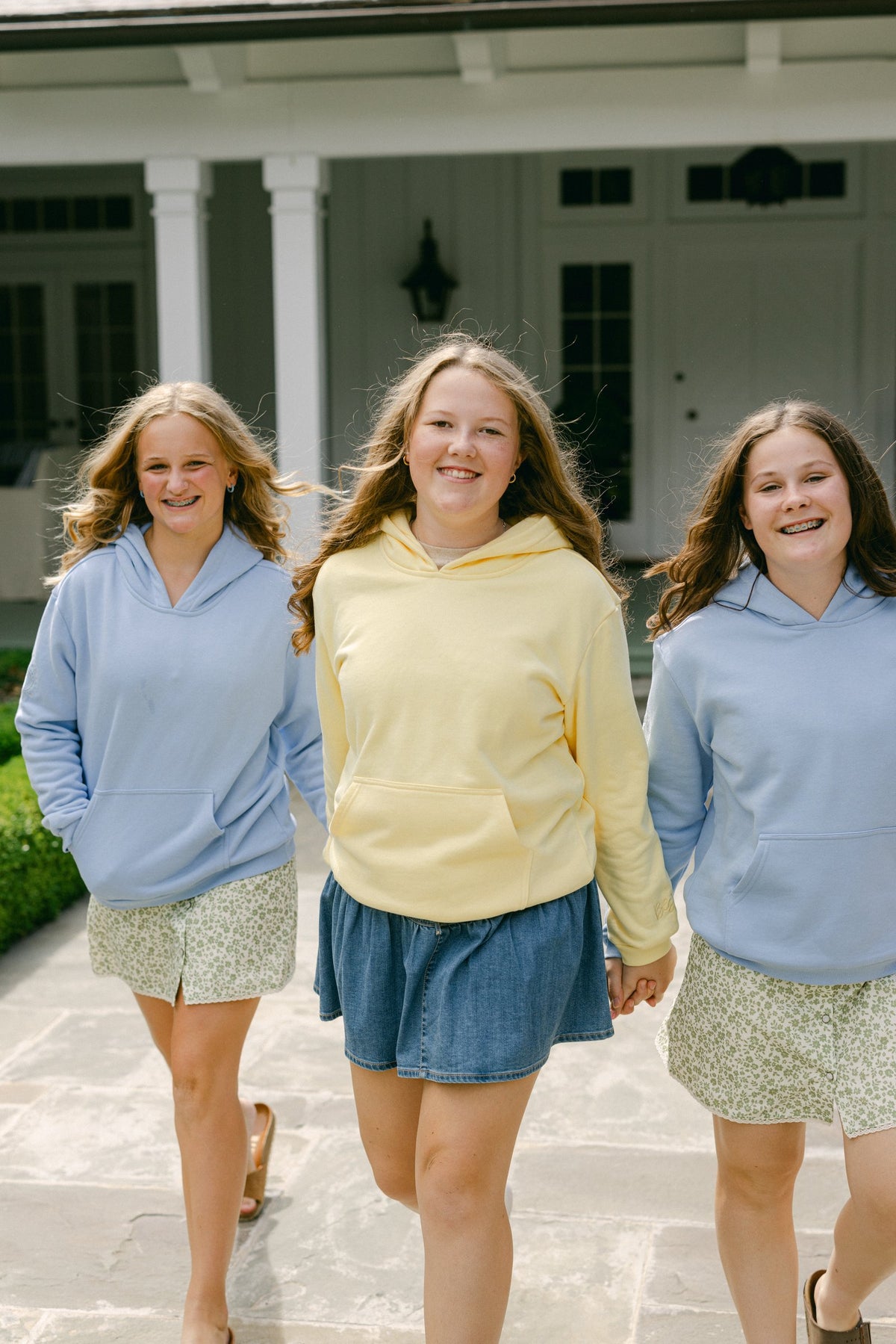 Three girls in hoodies holding hands and walking toward the camera