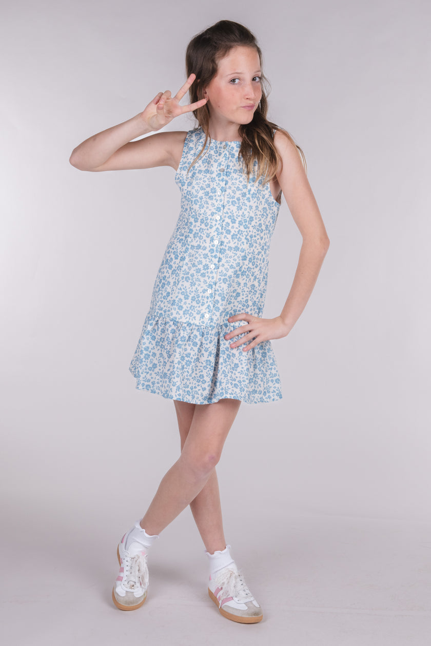 Tween girl wearing a blue floral tiered mini dress with white sneakers