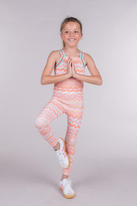Tween girl in tree pose wears orange and pink chevron print leggings with a matching crop top