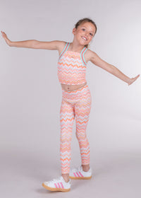 Tween girl wearing orange chevron print yoga tank and matching leggings arms outstretched