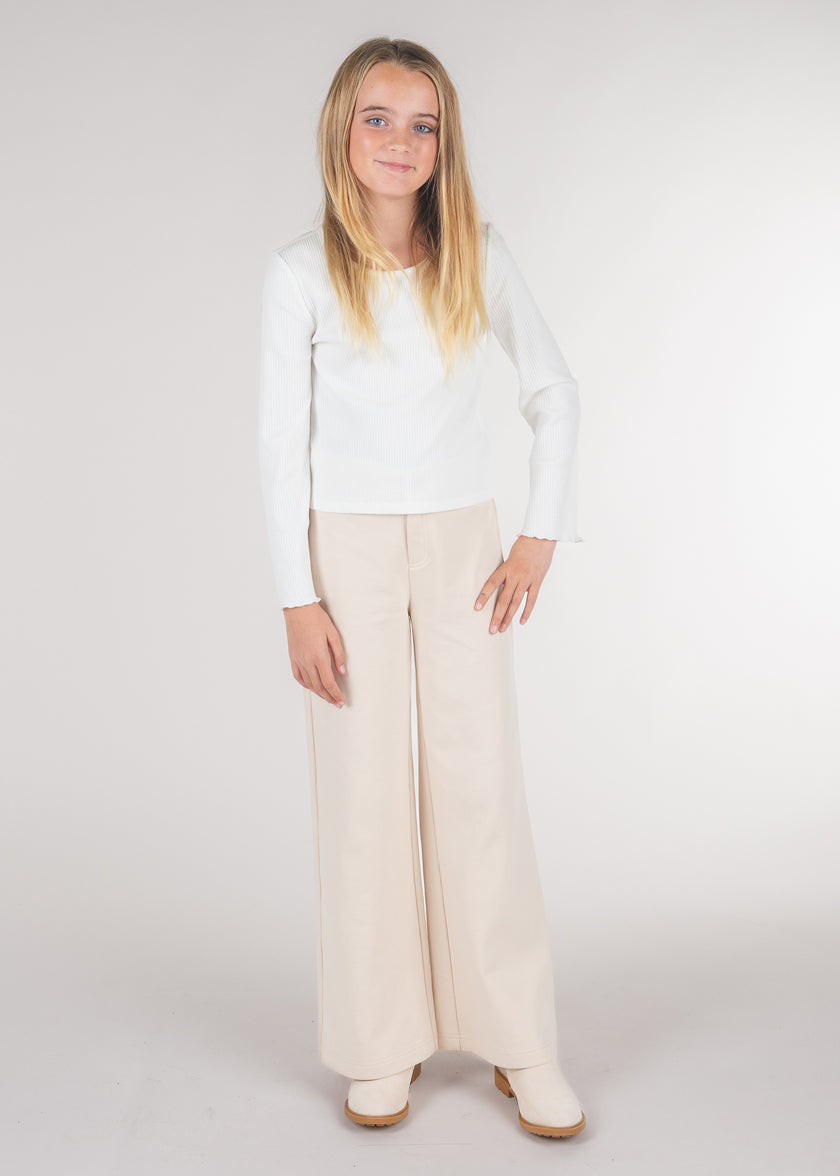 Tween girl wearing cream wide leg pants with a white long sleeve top