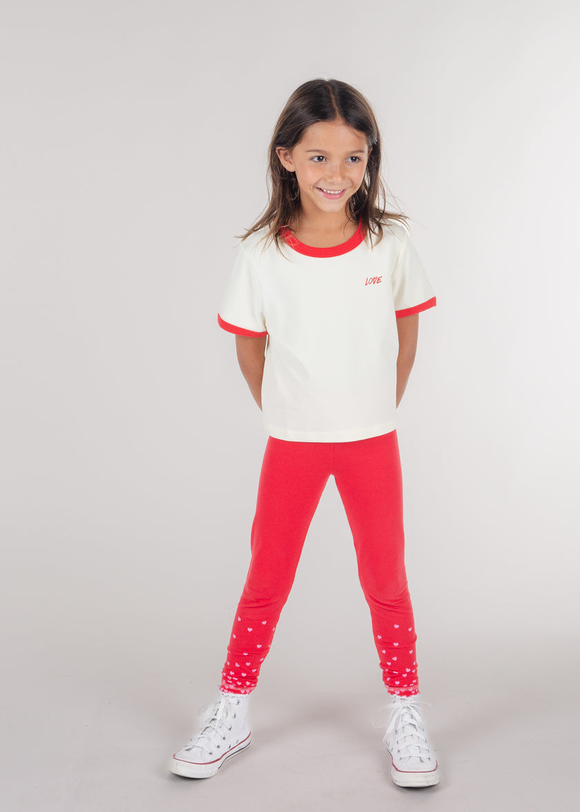 Tween girl smiling in an ivory ringer T-shirt with red trim and red leggings