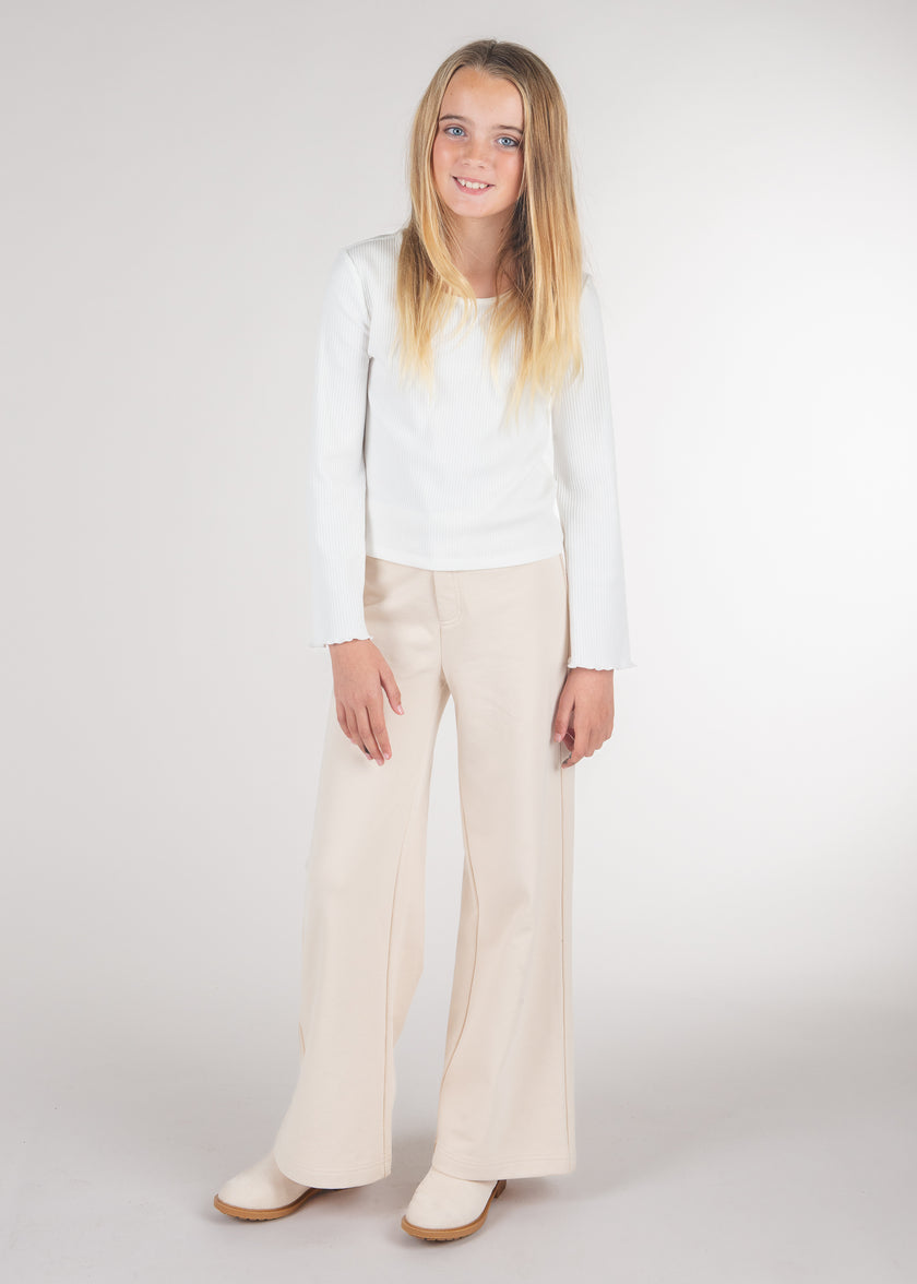 Tween girl wearing a white long-sleeve ribbed top with lettuce-hem cuffs