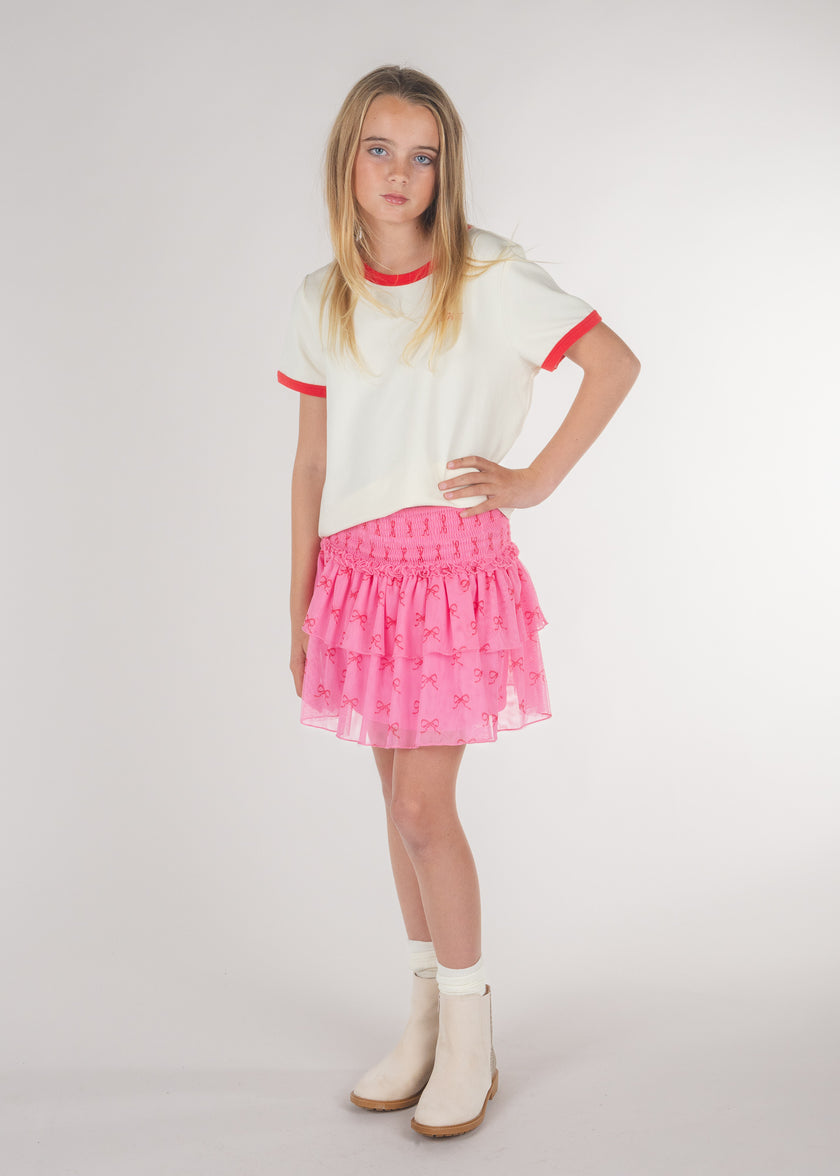 Tween girl wearing a pink tiered ruffle skirt with bow print and a white tee