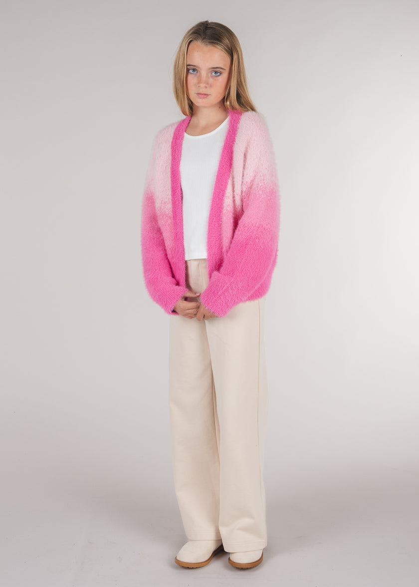 Tween girl wearing an open-front pink ombre fuzzy cardigan over a white top