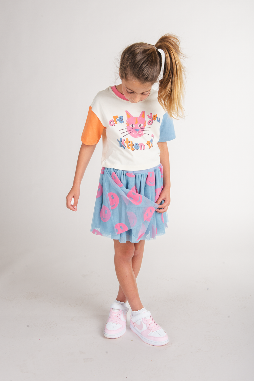 Tween girl wearing cream cat graphic tee with orange and blue sleeves and tulle skirt